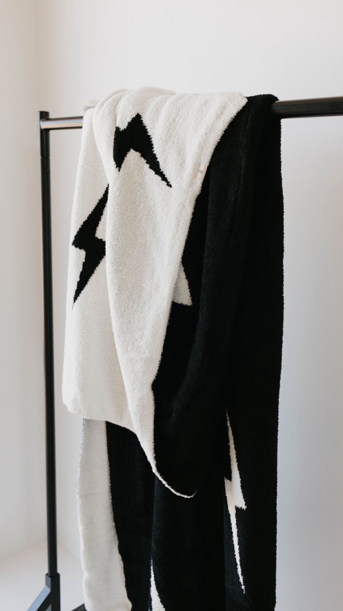 Cozy black and white lightning bolt plush blanket hanging on a rack, perfect for modern nursery decor.
