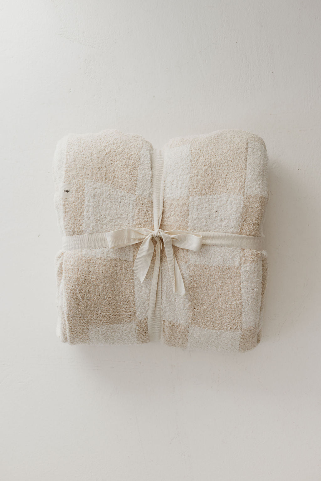 Cream checkerboard plush blanket tied with ribbon for cozy home decor, perfect for snuggling and gifting.