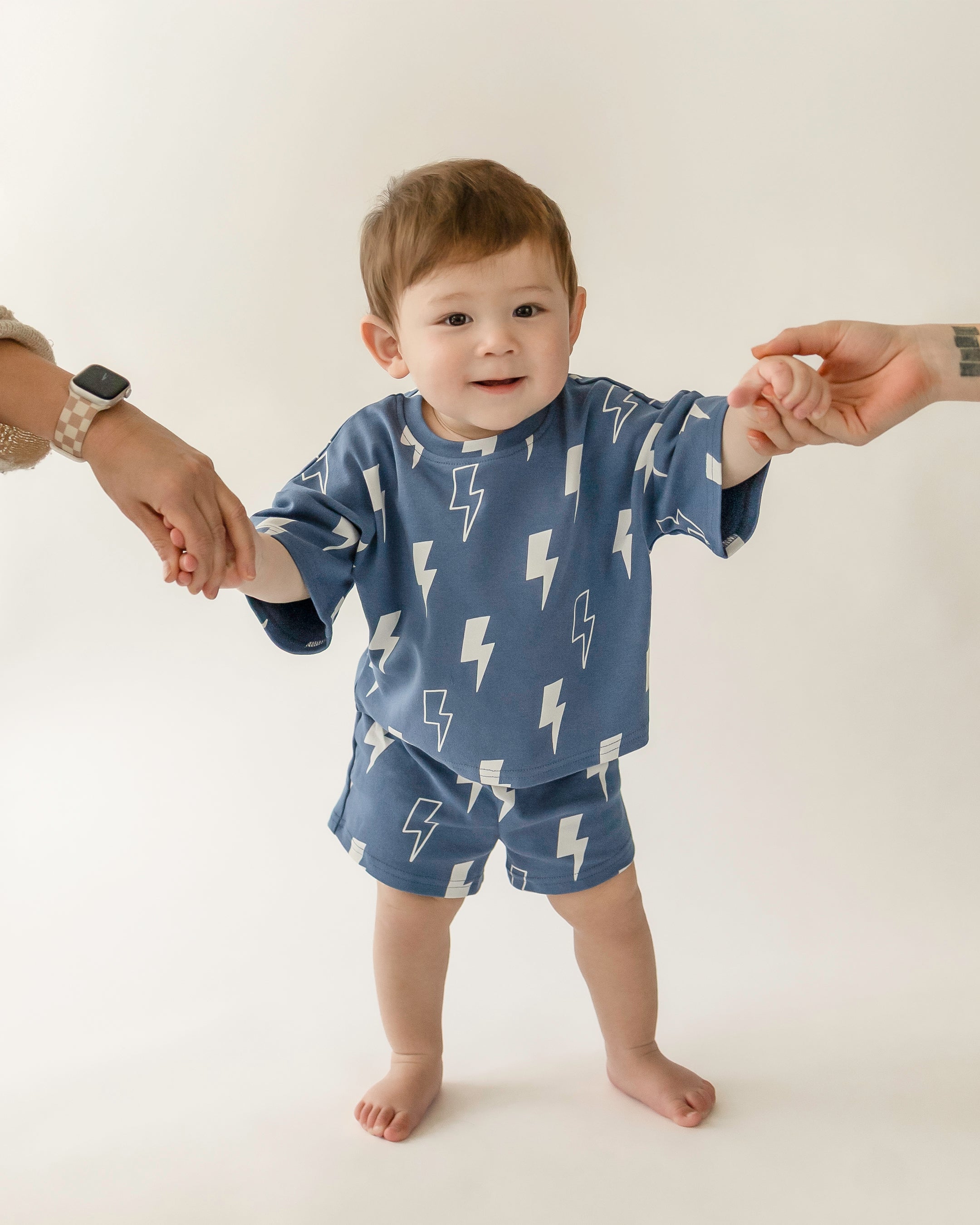 Child in blue bolt patterned shorts set, held by parents, showcasing fun style and comfort for kids.