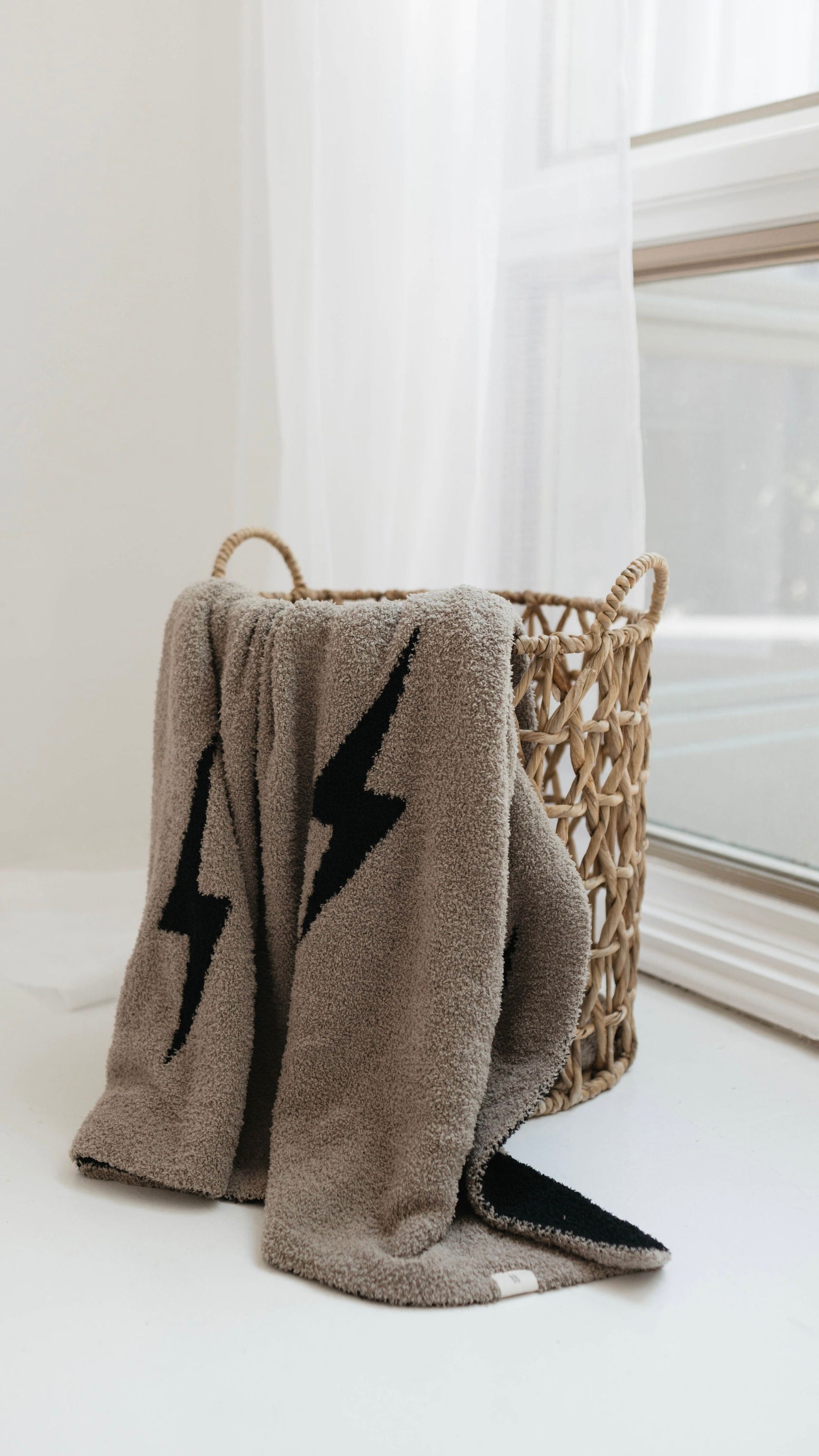 Cozy plush blanket with black lightning bolt pattern draped over a basket in a sunlit room.